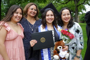 Four women, one of whom just graduated, smile while standing on the campus mall.