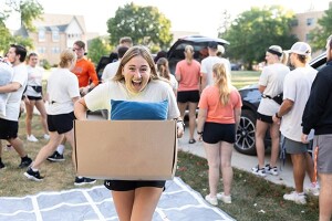 A female student brings a box of belongings into a residence hall.