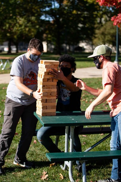 masked students play jenga on a picnic table outside.