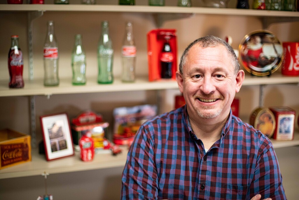 Kristopher Blanchard poses in front of his shelves lined with Coca-Cola bottles and other memorabilia
