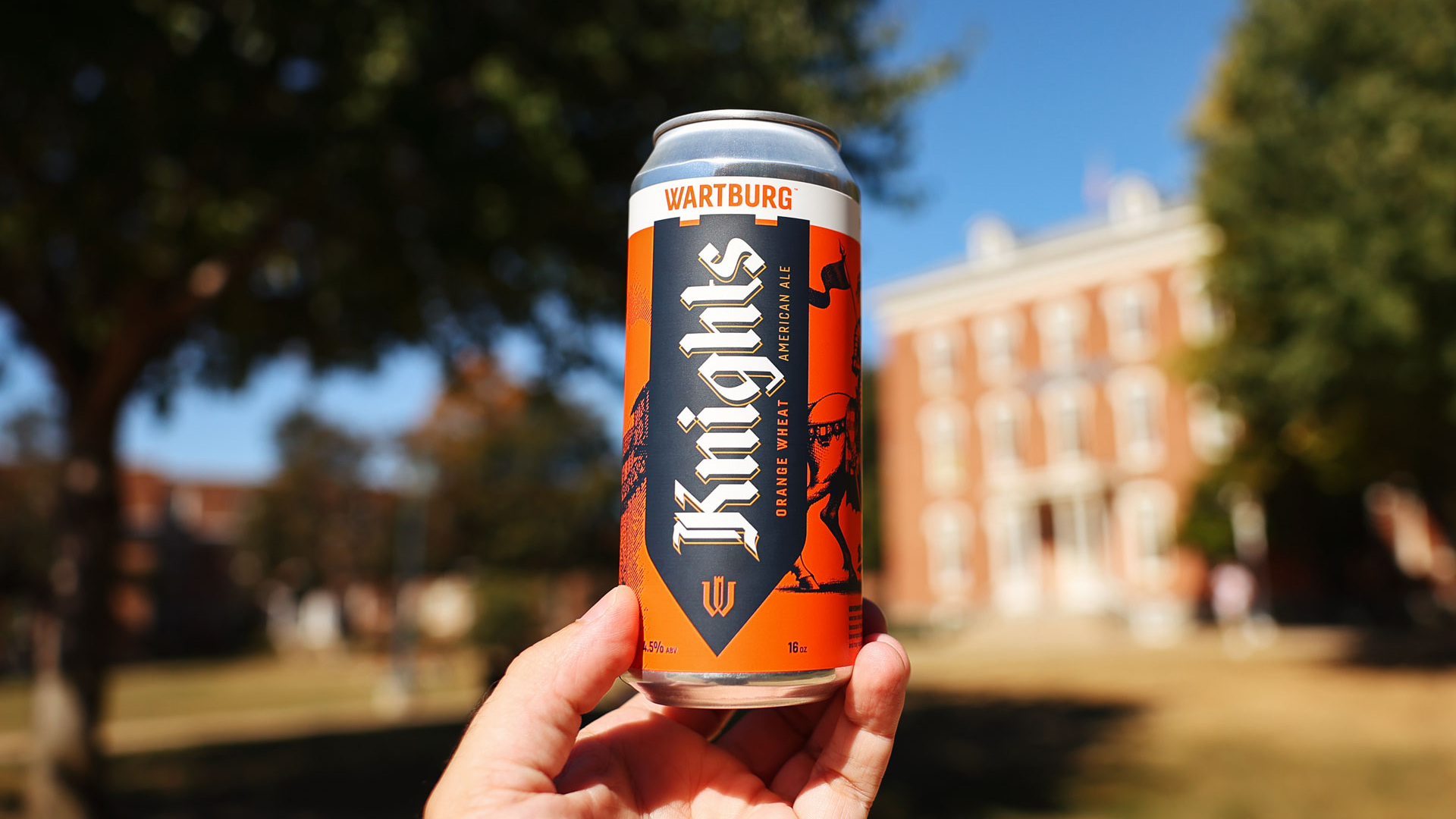 A can of Wartburg Knights Orange Wheat American Ale with Old Main in the background.