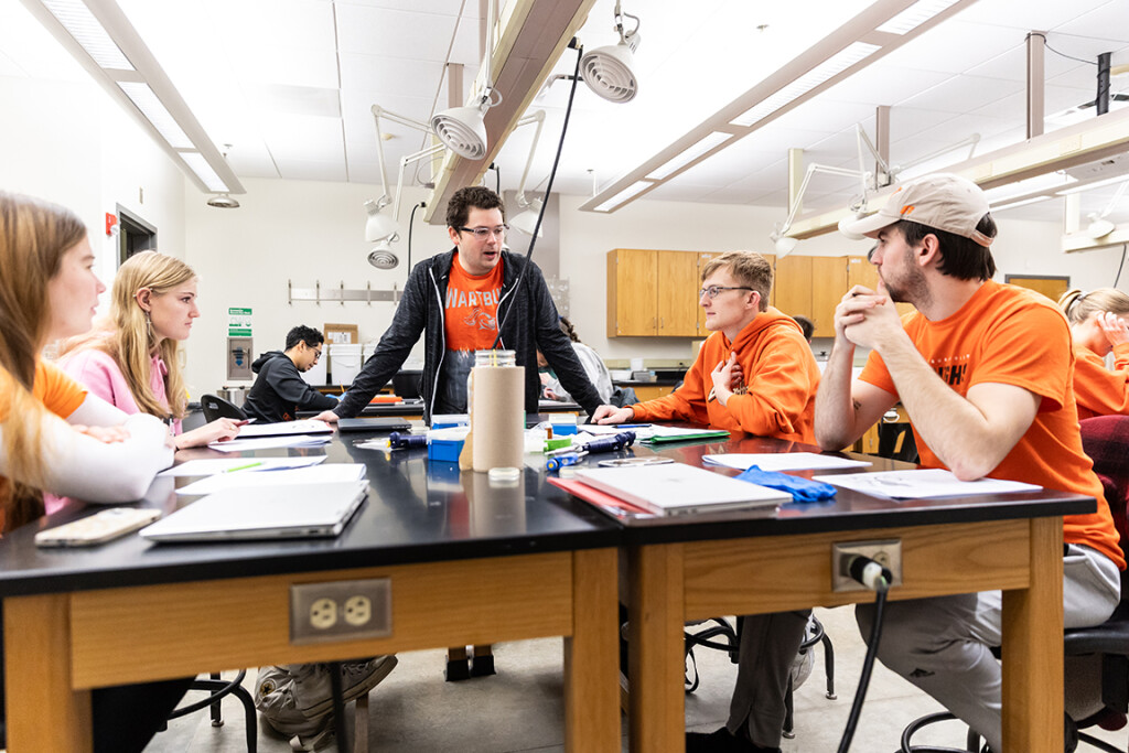 Dr. Cole Davidson speaks to four students seated at lab tables.