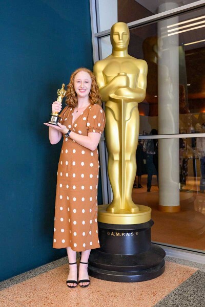 Lauren Ulveling holds an Oscar while standing next to a life size Oscar statue.