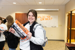 A Wartburg student smiles and holds a flag that says "Knights by a Million"