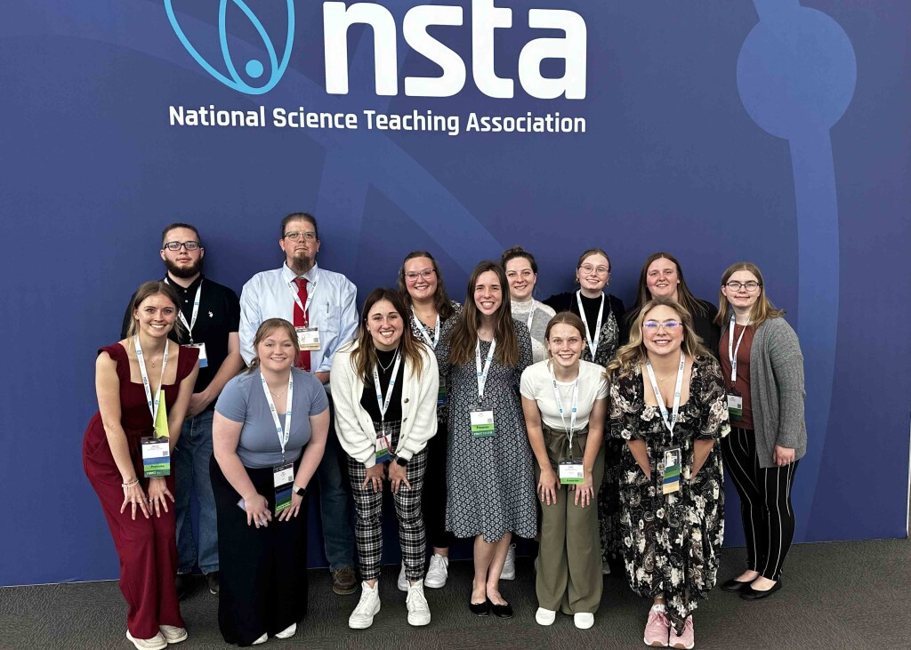 Wartburg college students and professor Michael Bechtel at the NSTA conference standing in front of the NSTA backdrop