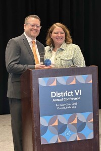Chris Knudson, left, and Sara Wald, District VI chair , stand behind a podium. Chris is holding his distinguished service award.