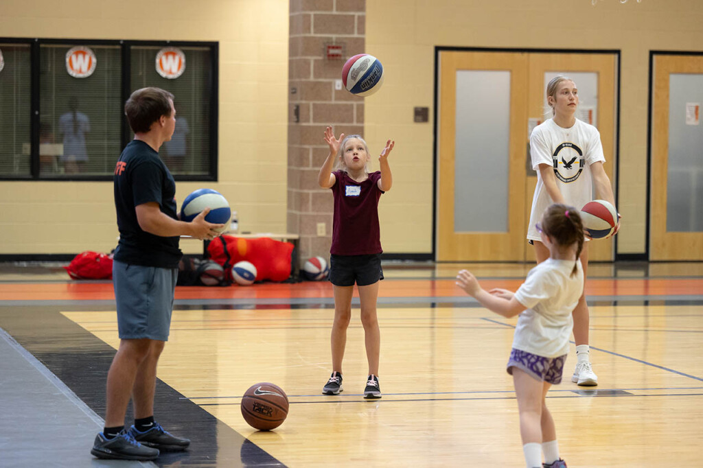 A young girl throws a basketball in the air while three others look on.