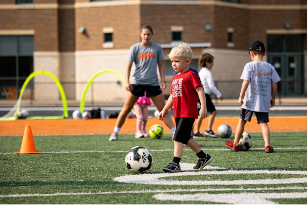 A small child prepares to kick a soccer ball as a Wartburg student supervises.