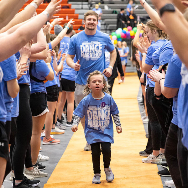 Owen Grover follows a young girl down the orange carpet through a tunnel of people during Wartburg College Dance Marathon.