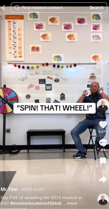 Phone screenshot from TikTok that shows Myles Finn on a stool in front of a white board with the names of musical posted on it. The text reads Spin that wheel.